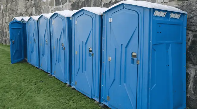 Row of blue portable toilets lined up on grass against a stone wall for event sanitation in Mesa, AZ